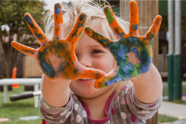toddler with hands covered in paint, smiling