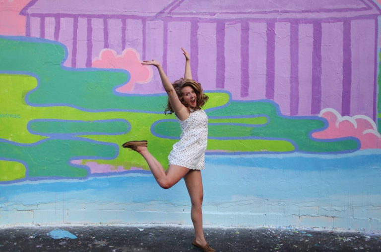 girl jumping in front of colourful wall with her arms in the air