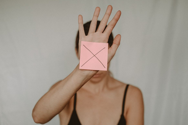 woman with her hand up and on her hand it a pink post-it note with an x drawn on it