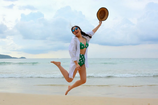 woman jumping on beach holding hat