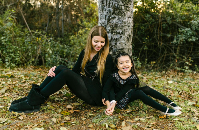mother and daughter sitting by a tree holding hands and smiling.