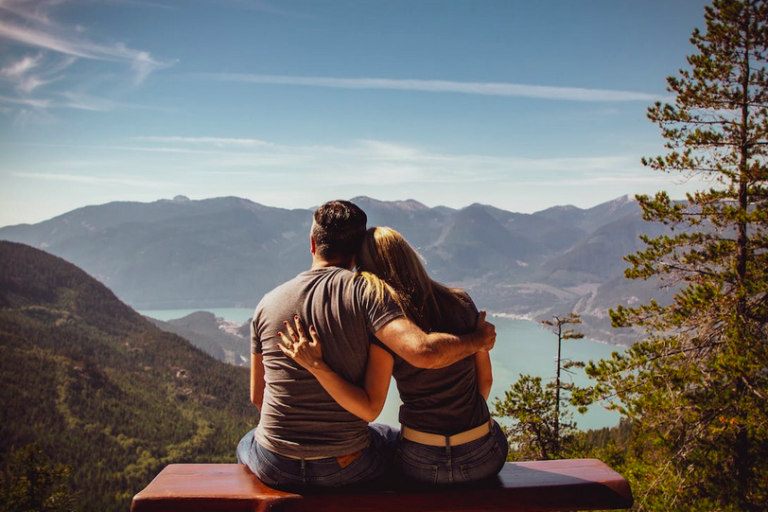 couple sitting on a bench atop a mountain looking at a river