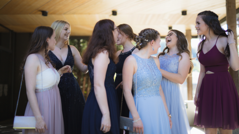 A group of teen girls wearing prom dresses laughing and smiling