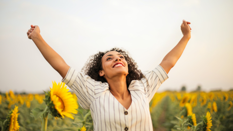 A woman raises her arms triumphantly in a field of sunflowers.
